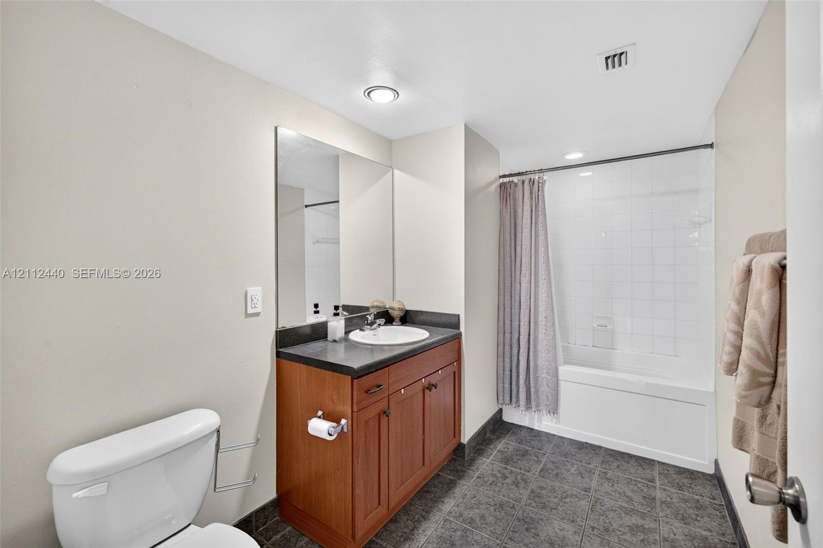 Bathroom featuring a wood look finish vanity with a dark countertop, and a tiled tub-shower combination with dark tile flooring