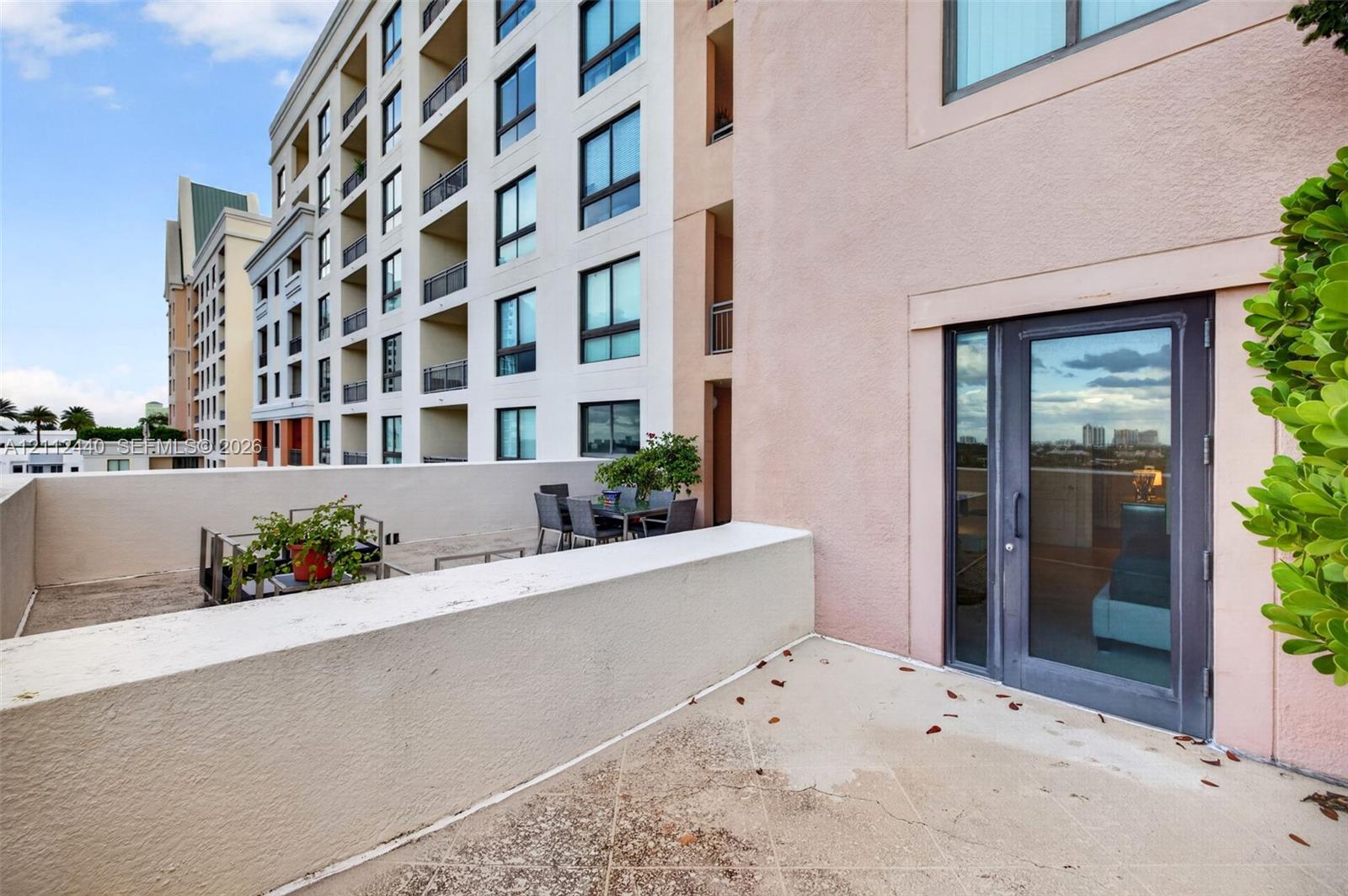 Expansive private terrace featuring concrete flooring and a solid stucco perimeter wall, accessed through a full-height glass door
