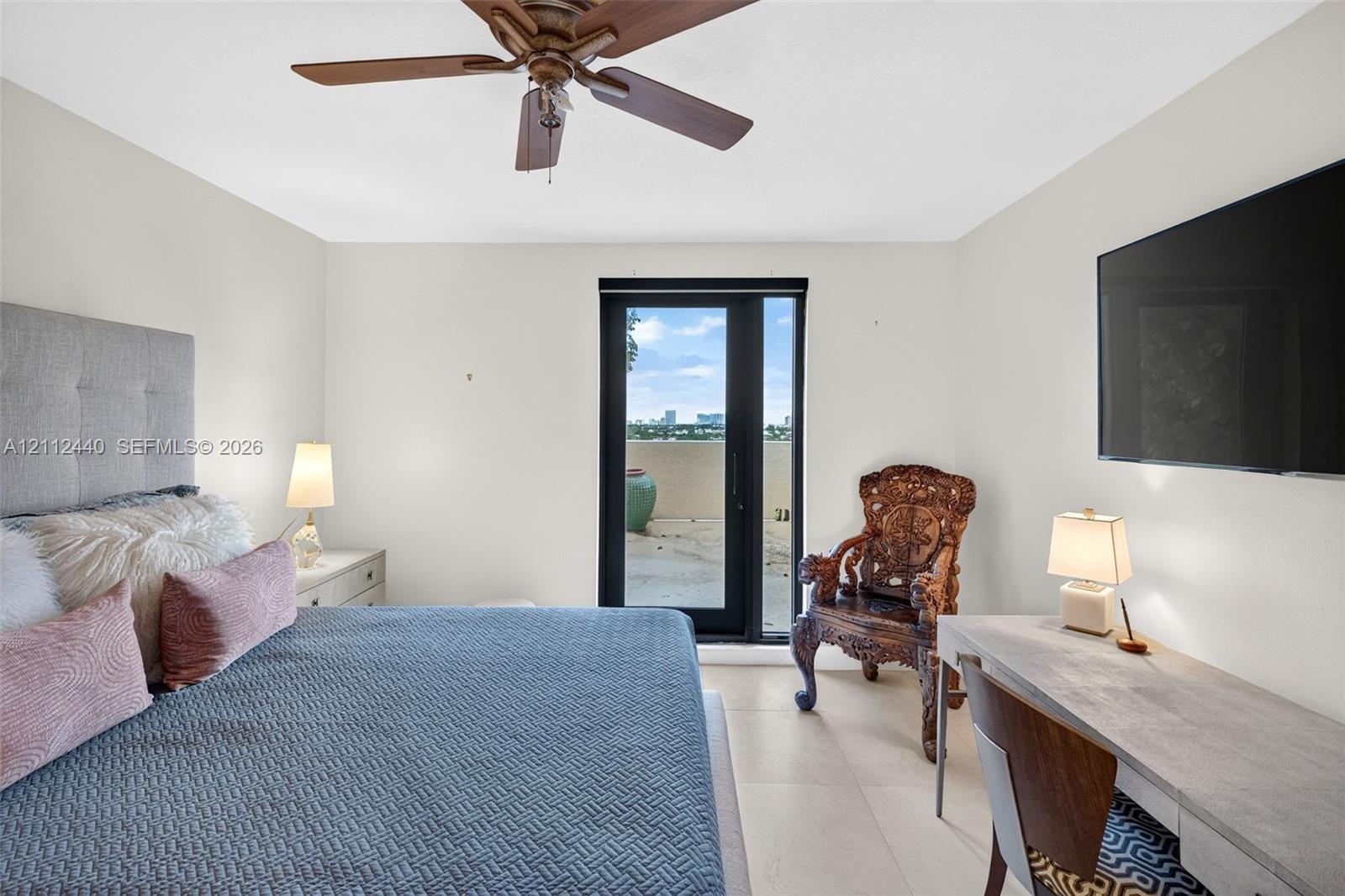 Neutral-toned interior featuring large-format porcelain flooring, a ceiling fan with integrated lighting, and a glass-paneled door opening to an oversized exterior terrace