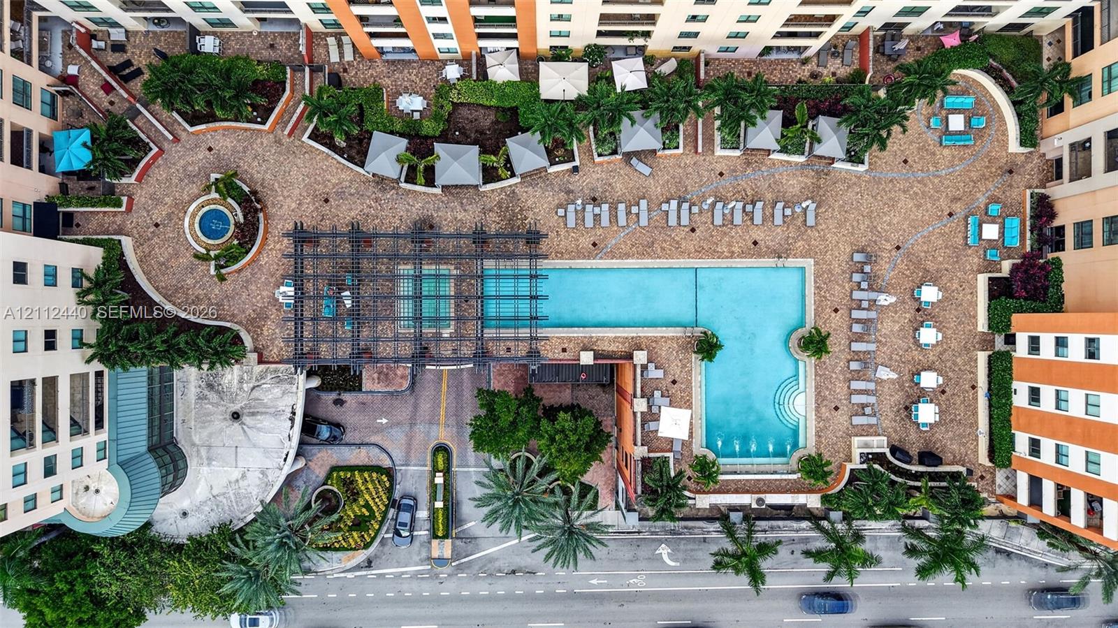 Aerial view of an expansive swimming pool, metal pergola, paver hardscaping, built-in water feature, and mature palm landscaping