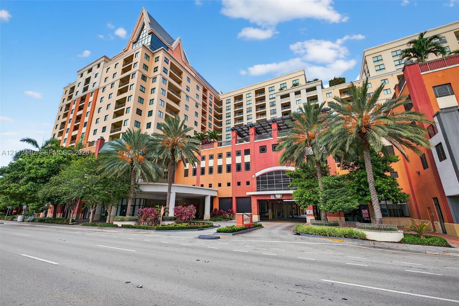 High-rise building featuring private balconies, a porte-cochre entryway, and mature palm tree landscaping