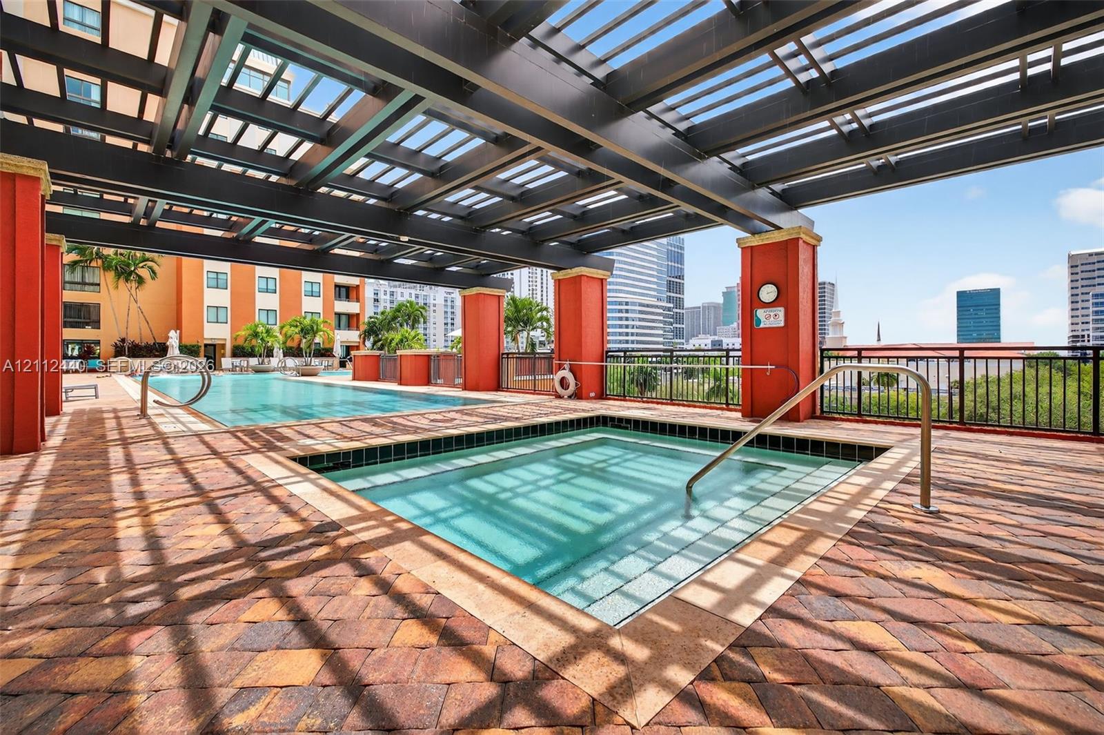 Covered pool and spa area featuring a dark-finish pergola, paver decking, and metal railings