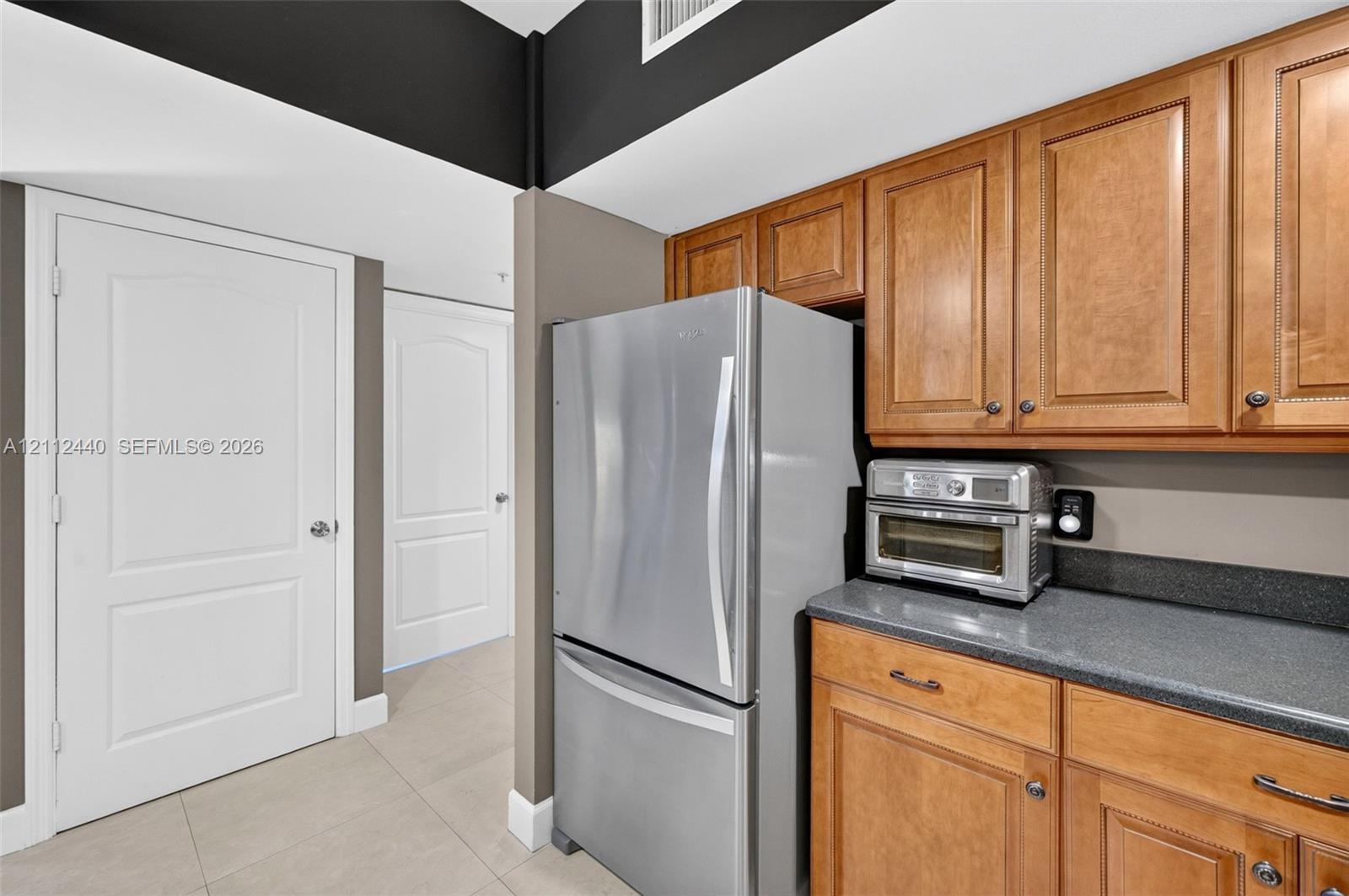 Kitchen featuring wood cabinets, stainless refrigerator, dark countertops, porcelain flooring