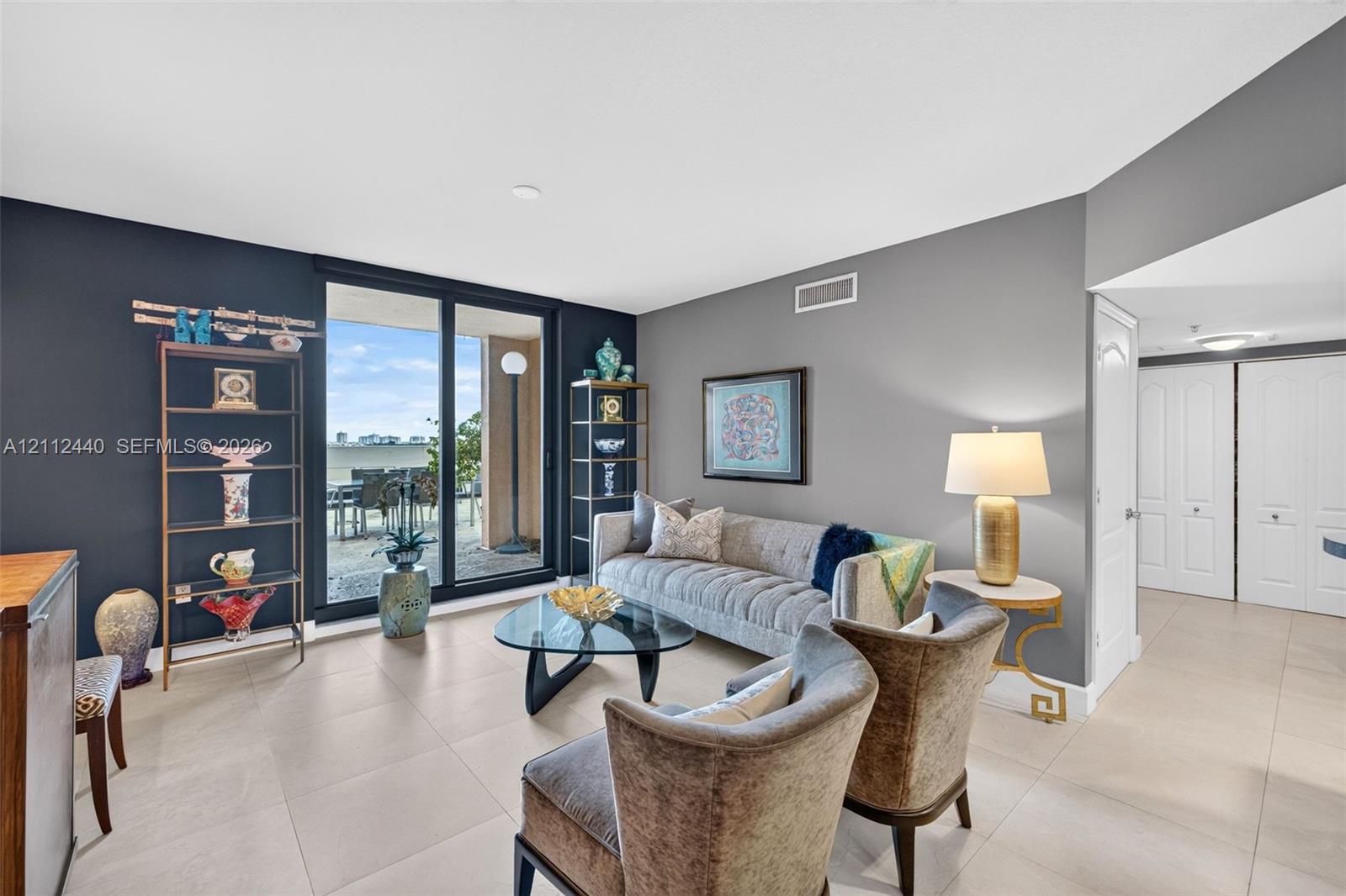 Living space featuring large-format neutral porcelain tile, dual-tone painted walls, and sliding glass doors opening to an oversized exterior balcony