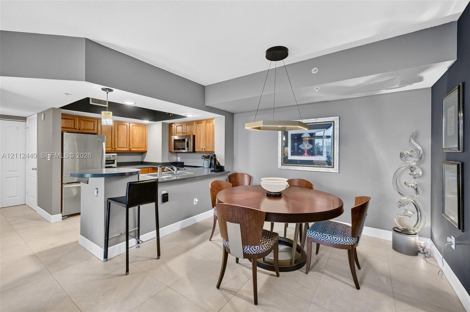 Kitchen featuring upgraded wood cabinets, stainless appliances, and a breakfast bar, complemented by large-format porcelain flooring (dining fixture does not convey)