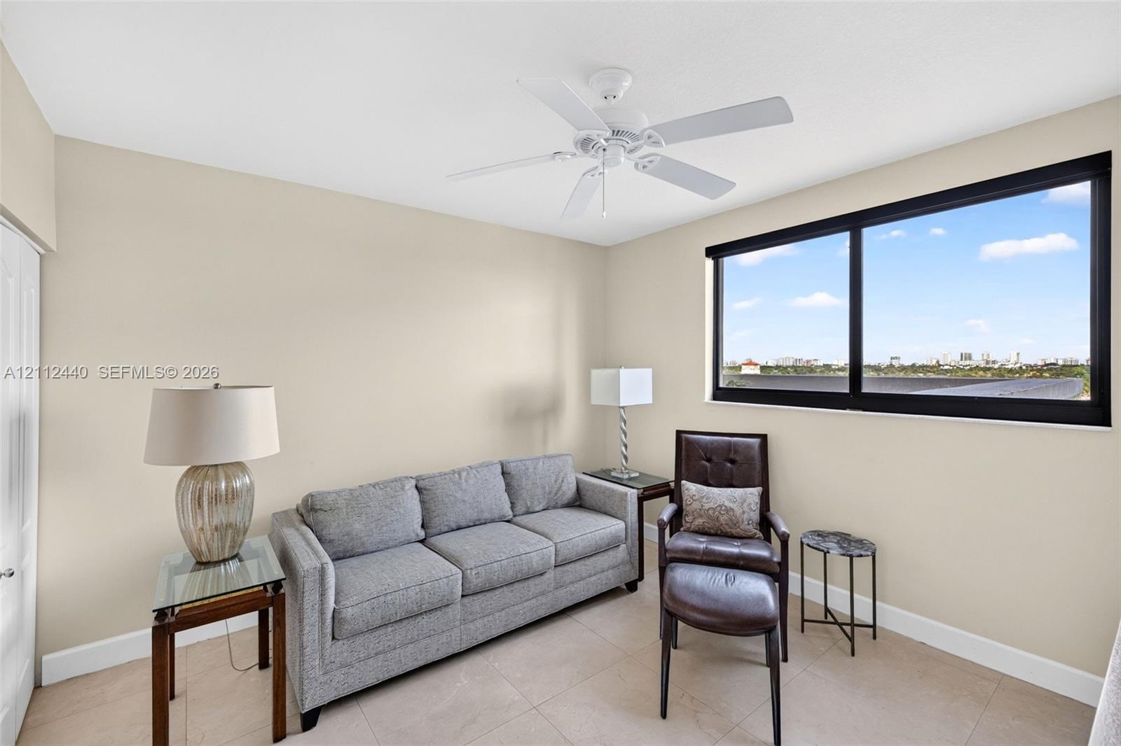 Neutral interior walls, large black-framed picture window, tile flooring, and white ceiling fan with light fixture