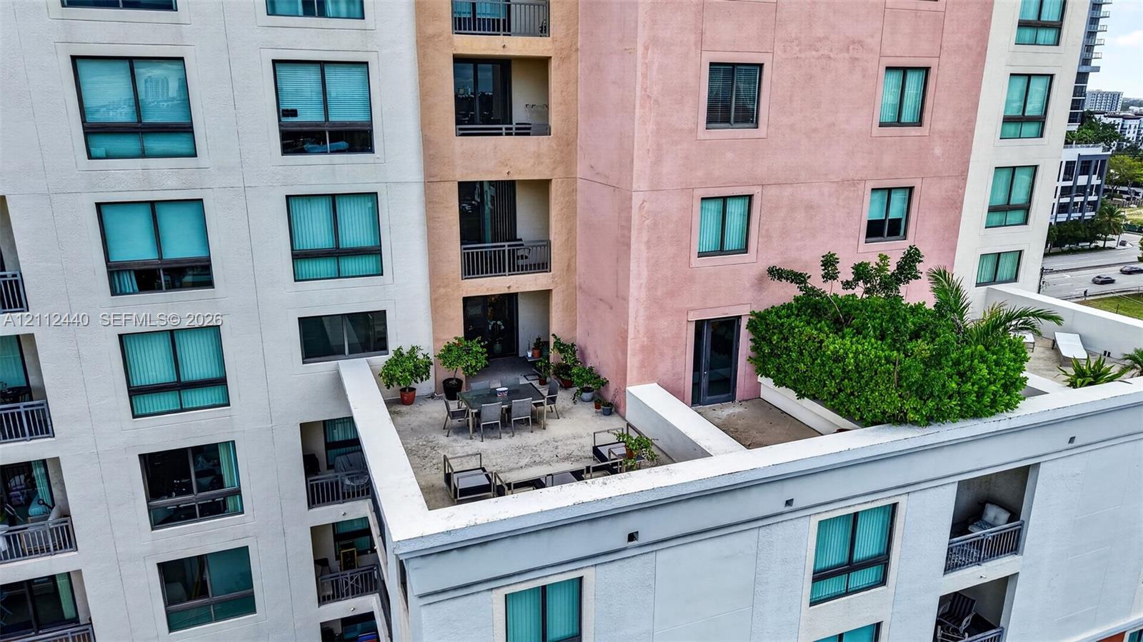 High-rise exterior featuring multi-colored stucco facade, expansive concrete terrace, integrated privacy landscaping, and recessed private balconies