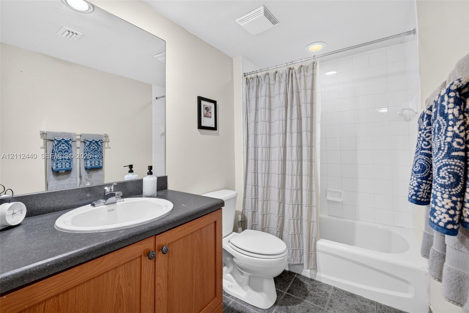 Bathroom featuring a wood look vanity, dark counter, recessed lighting, and a white tiled tub/shower surround