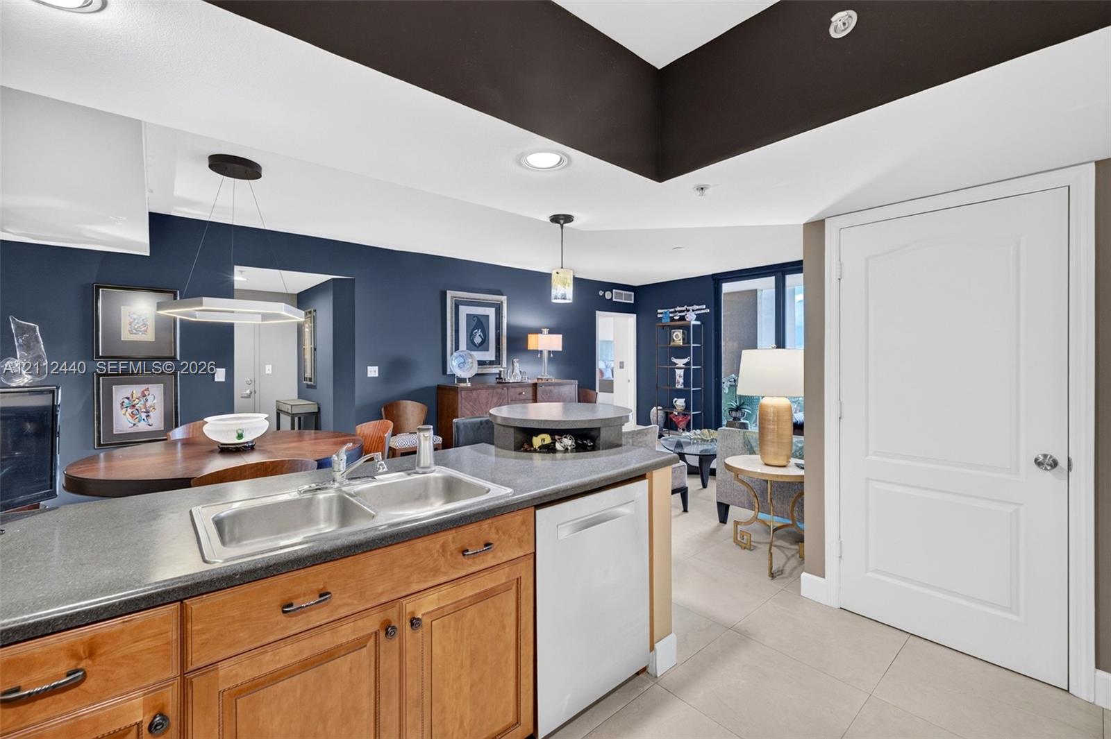 Kitchen featuring solid wood cabinetry, dark countertops, a stainless double-basin sink, recessed lighting, and a neutral porcelain floor