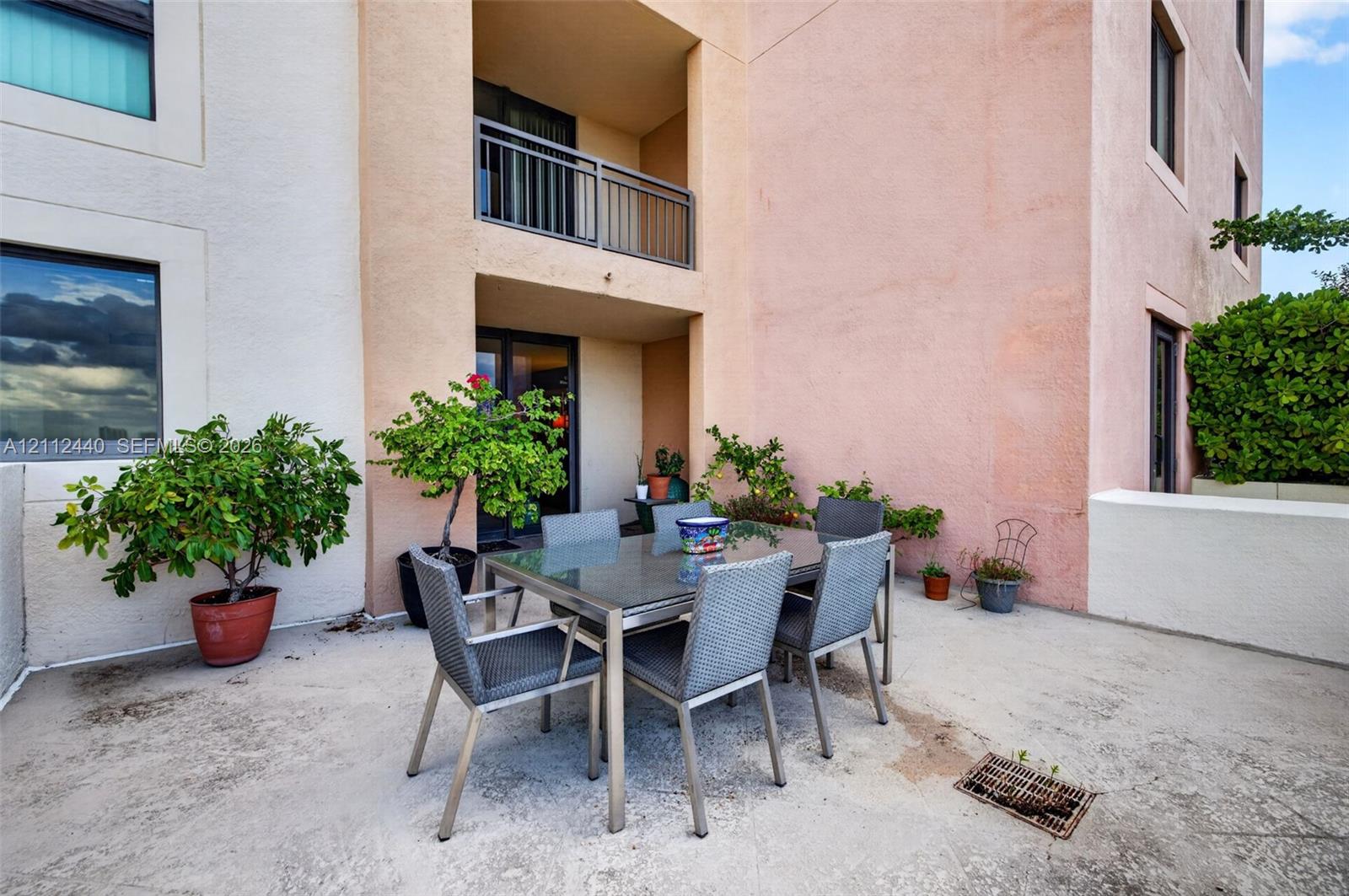 Spacious concrete patio featuring a stucco exterior, a covered balcony with a metal railing, and low-rise wall enclosures