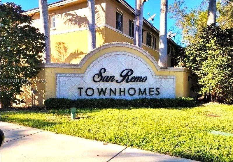 San Remo Townhomes monument signage featuring a stucco arched wall, decorative tile inlay, and landscaped grounds with mature palms San Remo Townhomes monument signage featuring a stucco arched wall, decorative tile inlay, and landscaped grounds with mature palms