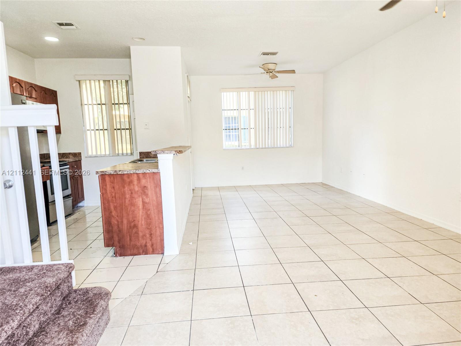 Open-concept floor plan featuring ceramic tile flooring, kitchen breakfast bar, wooden cabinetry, and dual ceiling fans Open-concept floor plan featuring ceramic tile flooring, kitchen breakfast bar, wooden cabinetry, and dual ceiling fans