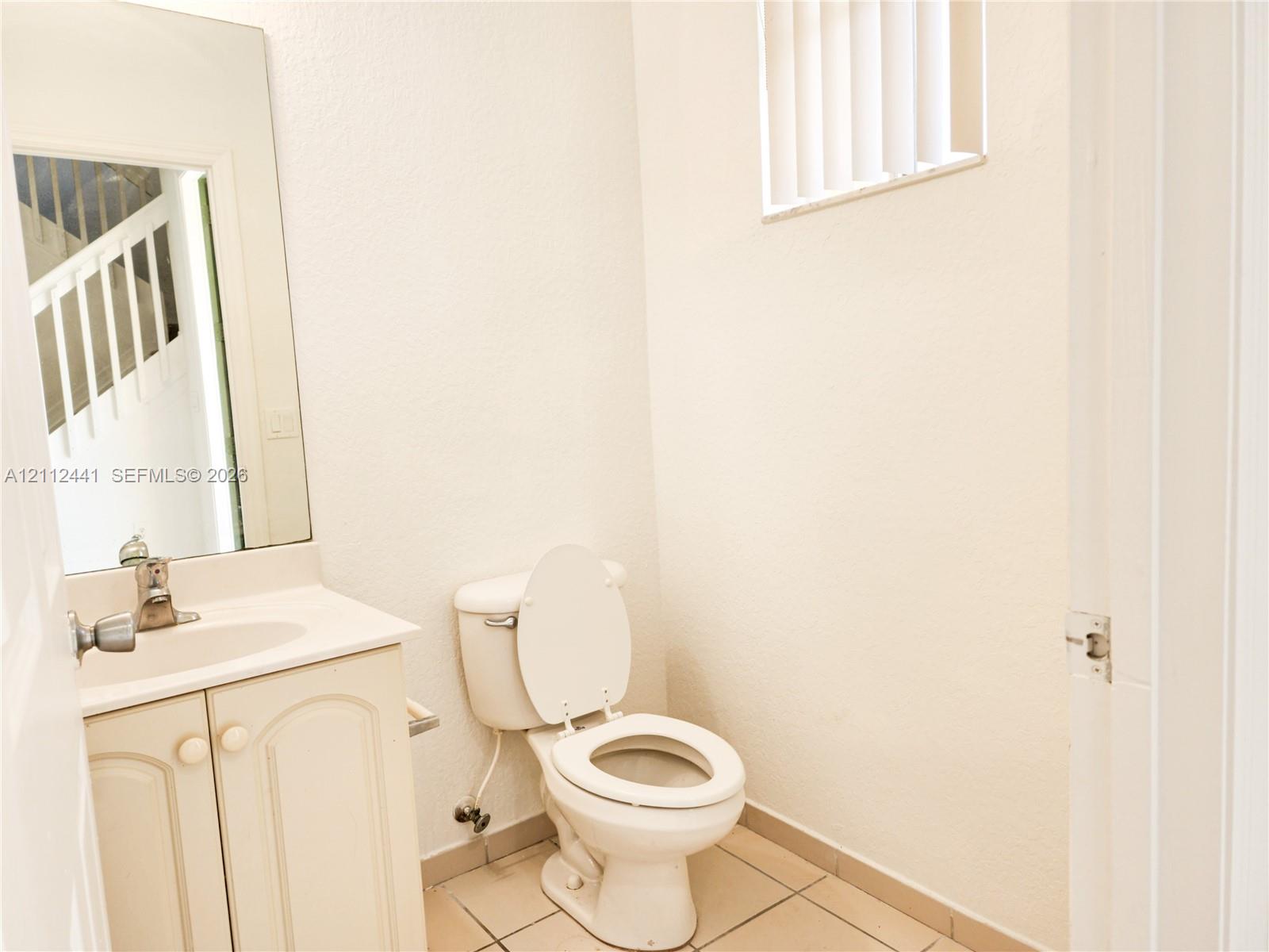 Vanity featuring cabinet storage and a sink basin, white toilet, wall-mounted mirror, and tile flooring Vanity featuring cabinet storage and a sink basin, white toilet, wall-mounted mirror, and tile flooring