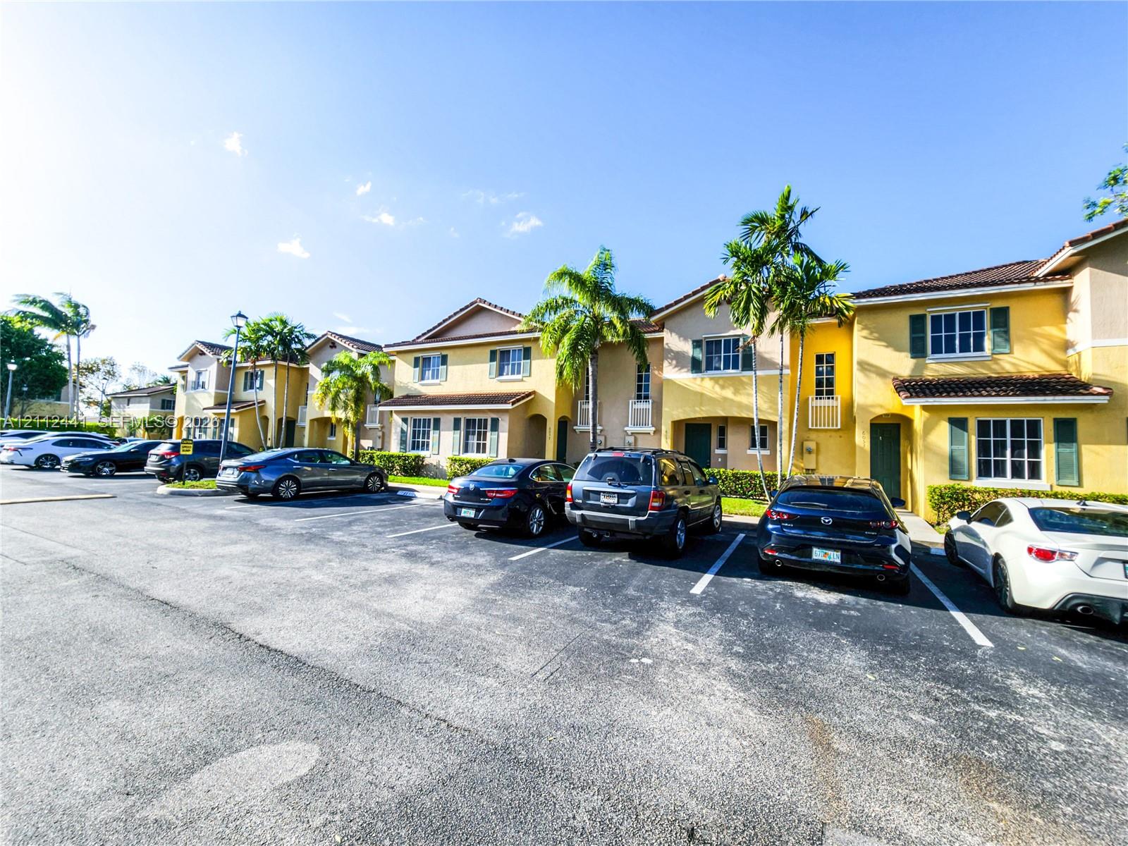 Two-story residential complex featuring stucco exterior walls, a shingled roof, decorative window shutters, and designated surface parking