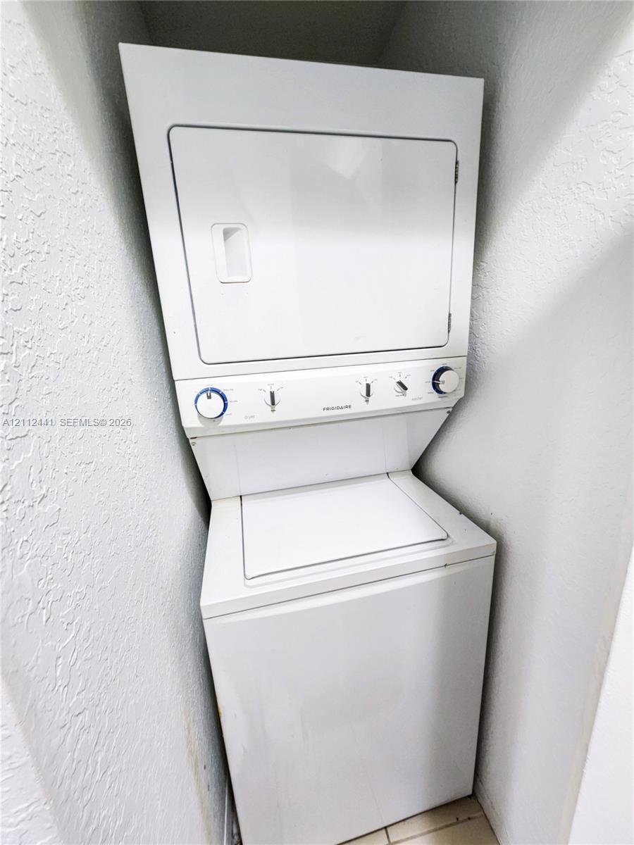 Stacked white laundry appliance featuring a top-loading washer and a dryer with manual rotary control dials