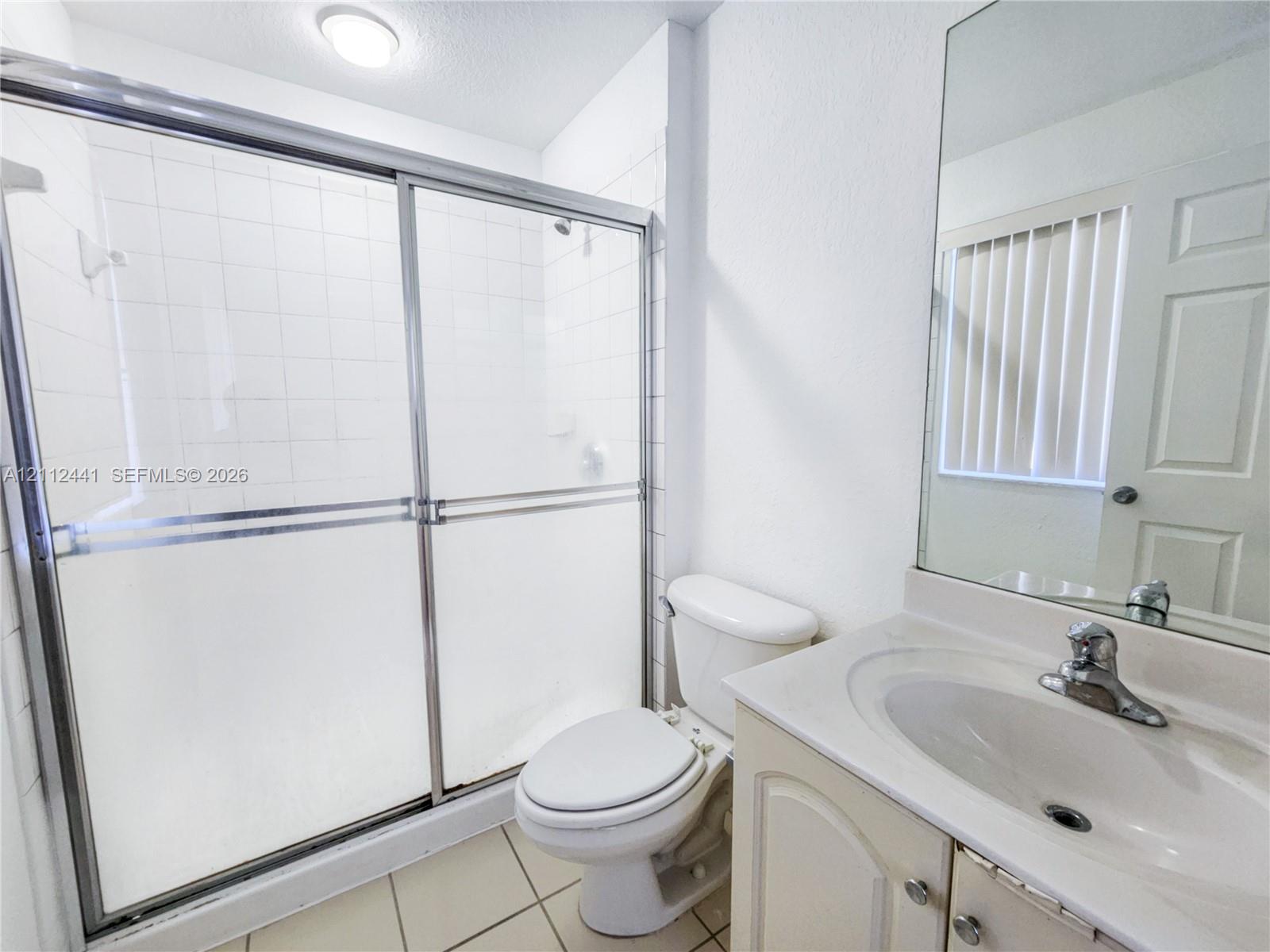 Bathroom featuring a walk-in shower with sliding glass doors, white tile surround, vanity with an integrated sink, and a wall-mounted mirror