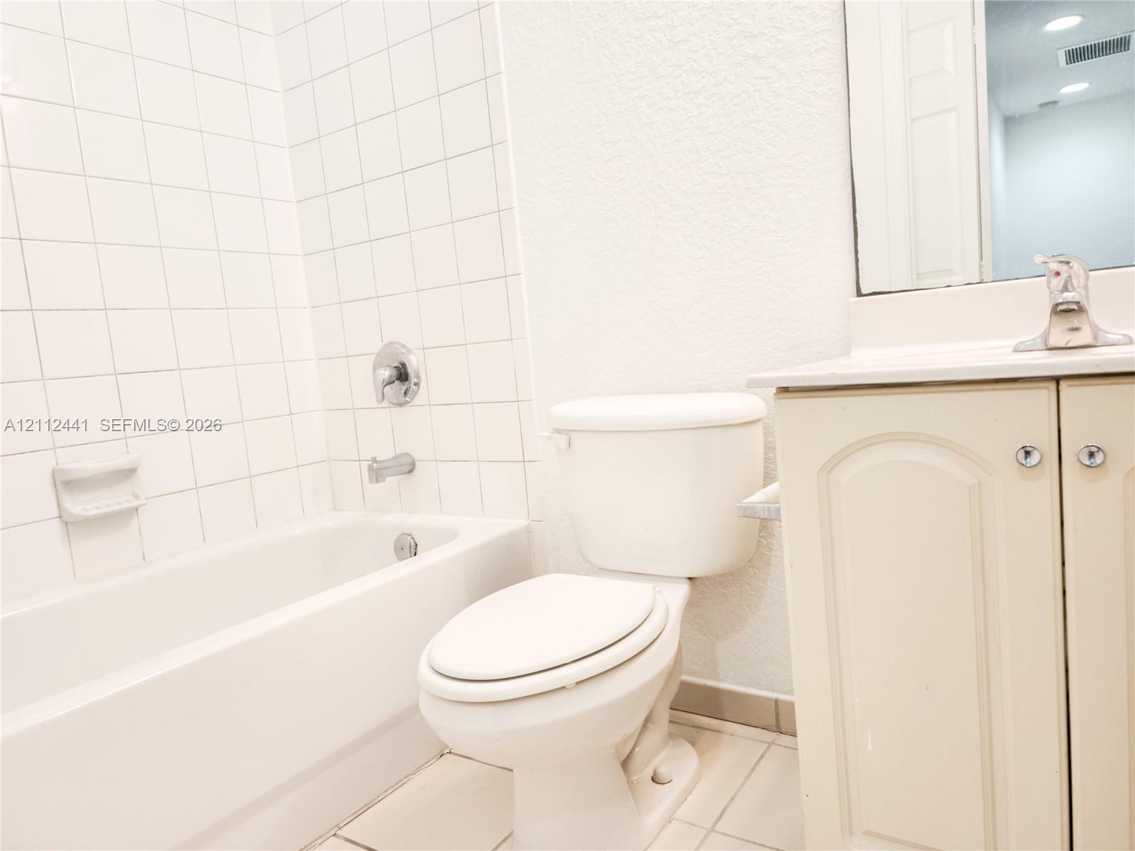 Bathroom featuring a white vanity cabinet with an integrated sink and chrome faucet, a bathtub with a white tile surround, and a wall-mounted mirror