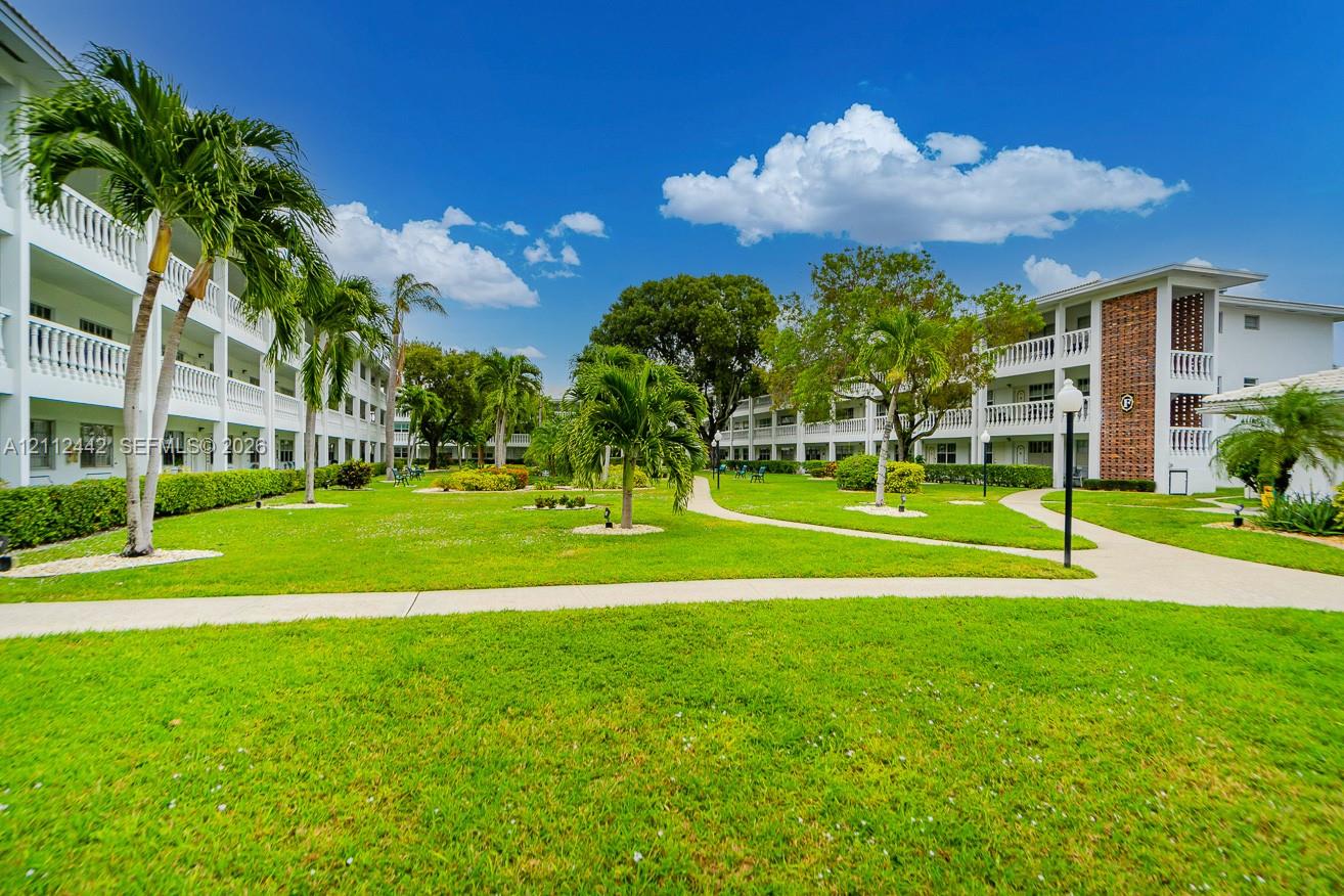Expansive central courtyard featuring manicured lawn, paved walkways, mature palm trees, and multi-story buildings with white balcony railings