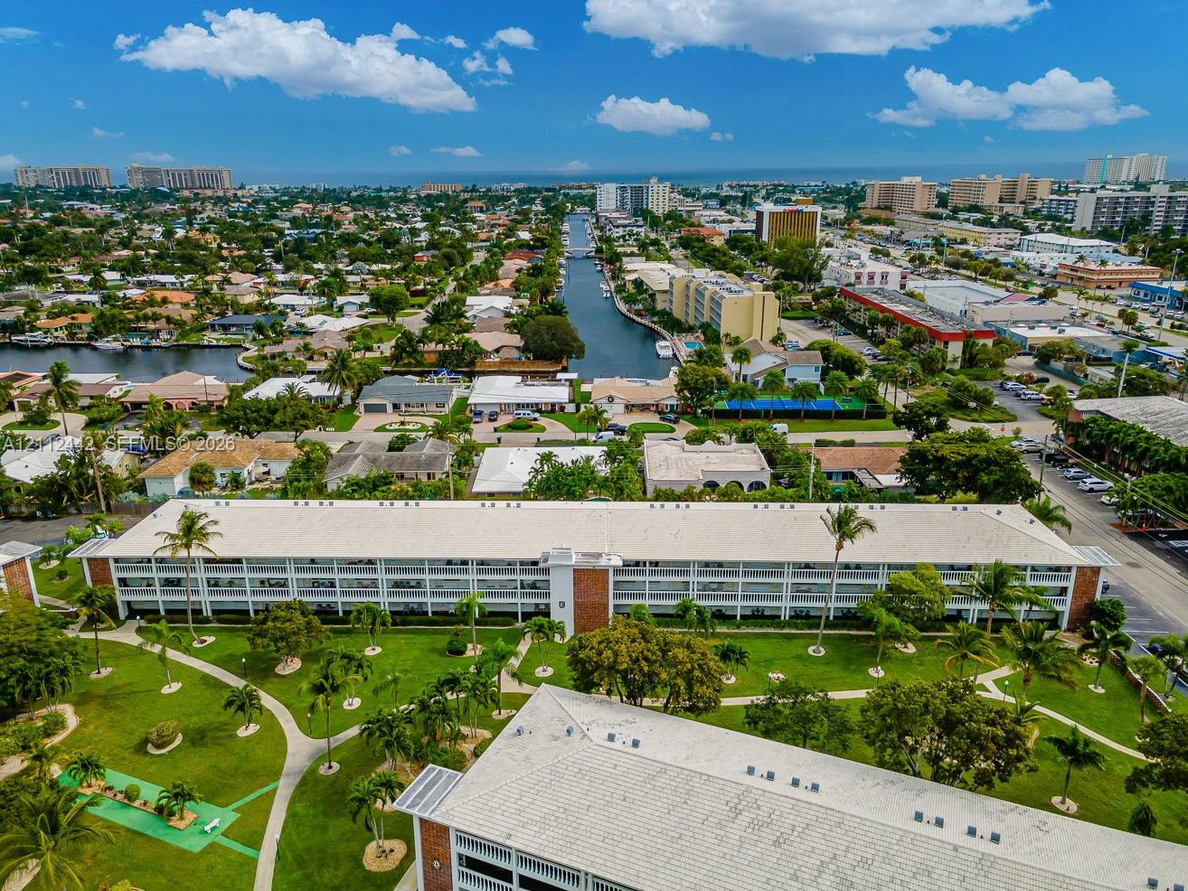 Aerial perspective of a multi-story residential building featuring exterior corridors, a metal roof, landscaped grounds, winding concrete walkways, and a miniature putting green