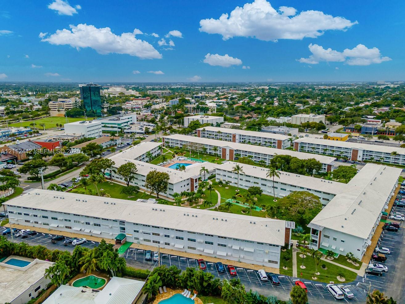 Aerial perspective of a multi-building residential complex featuring a central courtyard, landscaped green space, an outdoor swimming pool, and dedicated parking areas