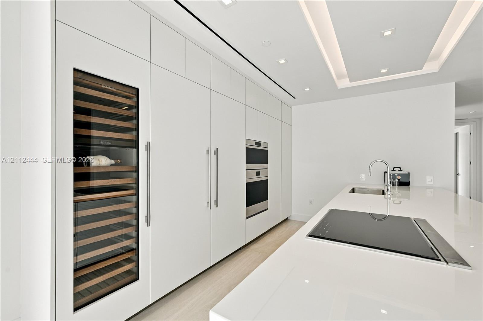 Sleek kitchen featuring custom floor-to-ceiling cabinetry, built-in stainless steel appliances, a glass-front wine refrigerator, and a solid-surface island with an integrated cooktop and undermount sink