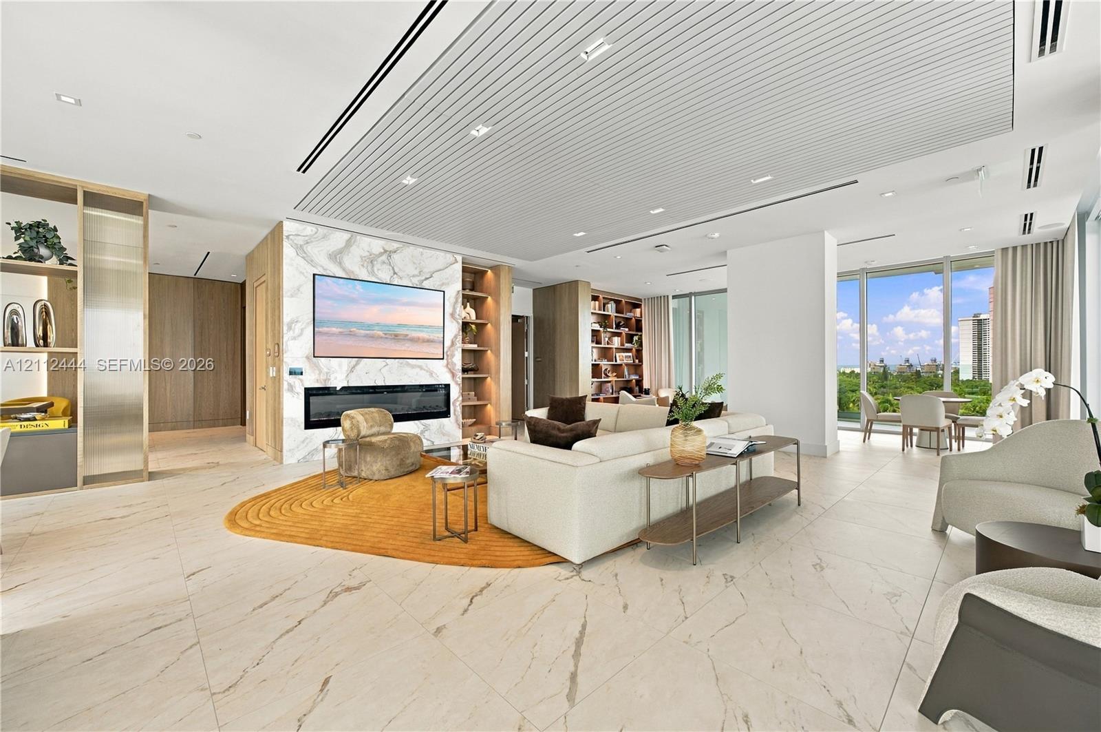 Open-concept interior featuring large-format tile flooring, a floor-to-ceiling stone-clad fireplace wall, custom built-in shelving, a tiered slatted ceiling with recessed lighting, and floor-to-ceiling windows