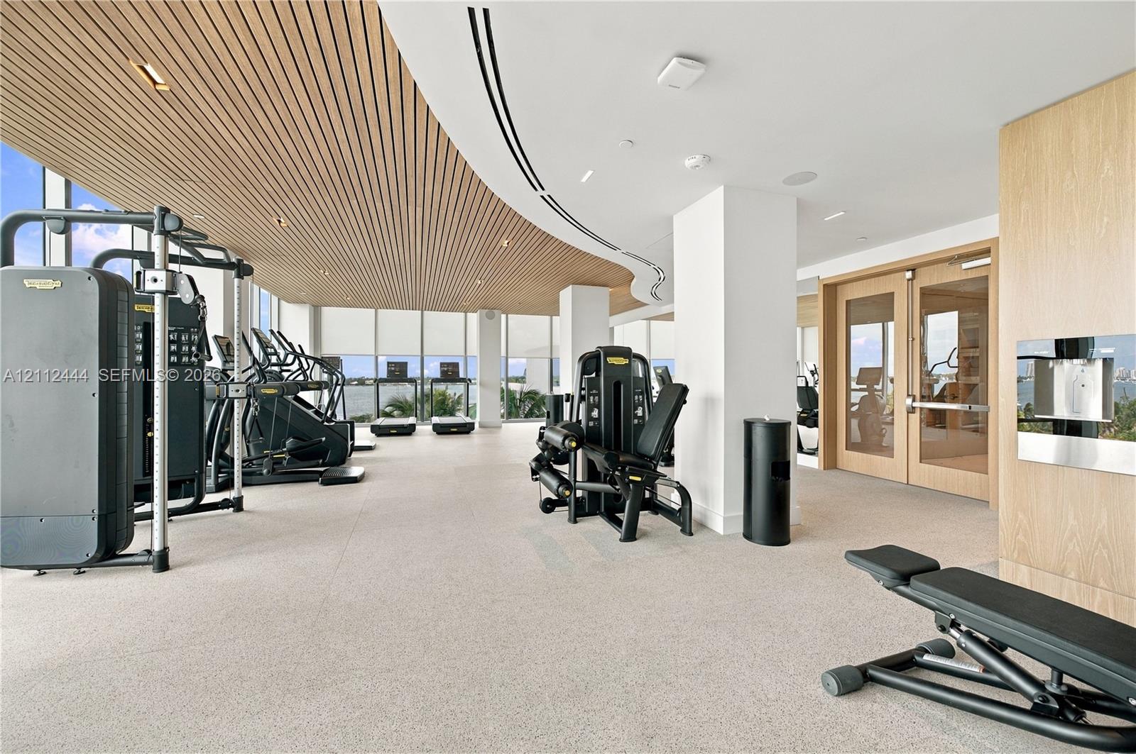 Fitness center featuring floor-to-ceiling windows, slatted wood-finish ceiling, recessed lighting, and wall-mounted water dispenser