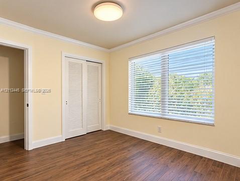Interior room featuring wood-finish flooring, crown molding, louvered closet doors, and a large window with fitted blinds Interior room featuring wood-finish flooring, crown molding, louvered closet doors, and a large window with fitted blinds