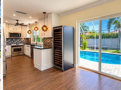 Kitchen featuring white shaker-style cabinetry, dark stone countertops, stainless steel appliances, built-in wine storage, and wood-finish flooring Kitchen featuring white shaker-style cabinetry, dark stone countertops, stainless steel appliances, built-in wine storage, and wood-finish flooring