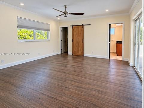 Spacious room featuring wood-finish flooring, a ceiling fan, crown molding, a wood-grain barn door with black hardware, and glass sliding doors