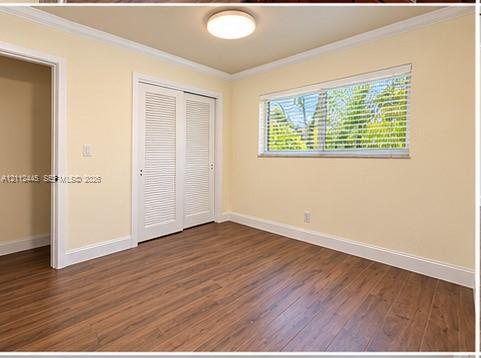 Interior room featuring wood-finish flooring, white louvered closet doors, a horizontal sliding window with blinds, crown molding, and a flush-mount ceiling light