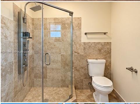 Walk-in shower featuring glass enclosure, rain-style showerhead, and integrated multi-function wall panel with natural stone-finish tile surround and flooring