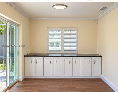Custom built-in white cabinetry featuring dark stone-finish countertops, wood-finish flooring, sliding glass door, and window with plantation-style shutters Custom built-in white cabinetry featuring dark stone-finish countertops, wood-finish flooring, sliding glass door, and window with plantation-style shutters