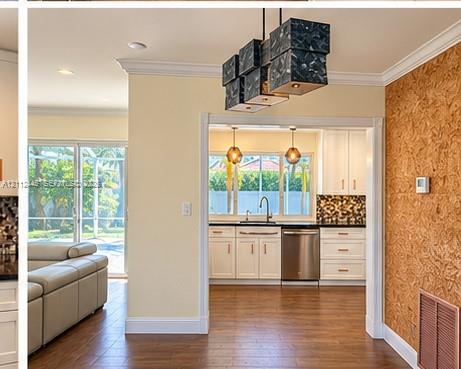Multi-light geometric chandelier, wood-finish flooring, crown molding, kitchen with white cabinetry, and textured wood-panel wall feature Multi-light geometric chandelier, wood-finish flooring, crown molding, kitchen with white cabinetry, and textured wood-panel wall feature