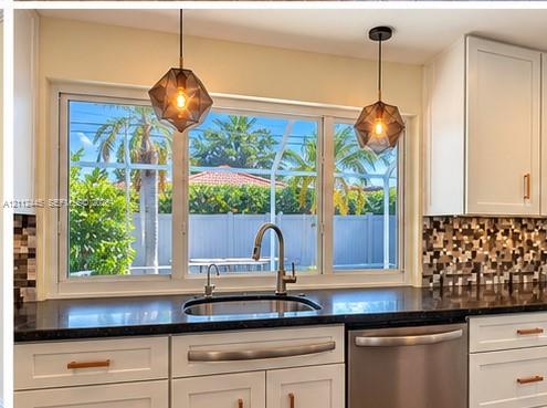 Kitchen featuring white cabinetry with metallic hardware, dark countertops, a mosaic tile backsplash, stainless steel sink with high-arc faucet, and geometric pendant lighting Kitchen featuring white cabinetry with metallic hardware, dark countertops, a mosaic tile backsplash, stainless steel sink with high-arc faucet, and geometric pendant lighting