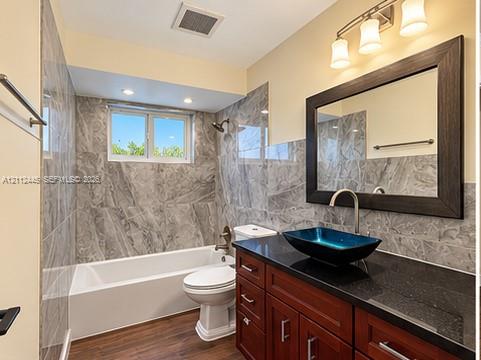 Full-height stone-finish wall tile, wood-finish cabinetry with a dark stone countertop, rectangular blue vessel sink, and an integrated three-light fixture