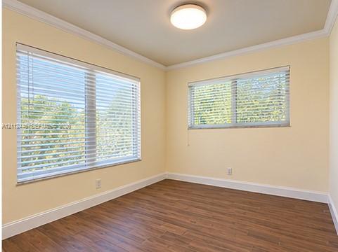 Room featuring wood-finish flooring, crown molding, two windows with horizontal blinds, and a flush-mount ceiling light