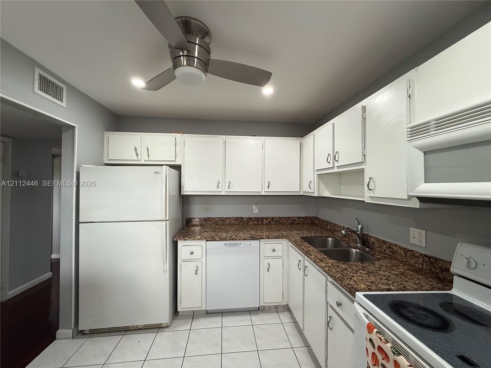 Kitchen featuring white cabinetry, stone-surface countertops, dual-basin stainless steel sink, tile flooring, and a ceiling-mounted fan Kitchen featuring white cabinetry, stone-surface countertops, dual-basin stainless steel sink, tile flooring, and a ceiling-mounted fan