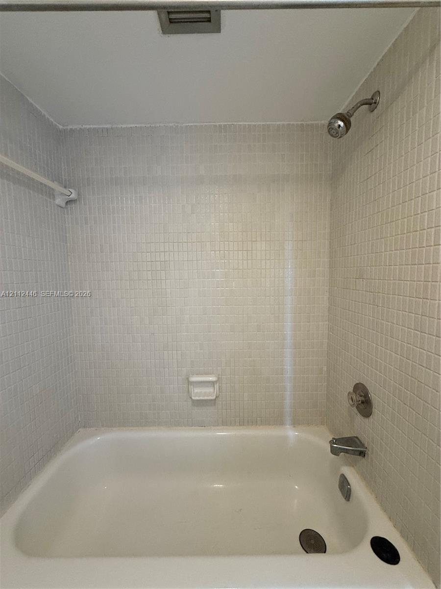 Bathtub featuring a white finish, wall-mounted shower head, integrated faucet, built-in soap dish, and neutral mosaic tile surround