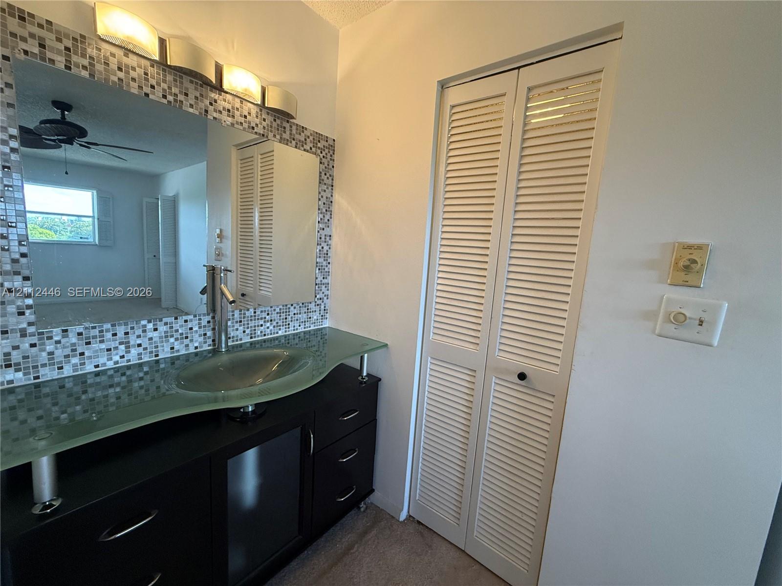 Black vanity featuring a glass vessel sink, chrome single-lever faucet, tiled mirror surround, and louvered bi-fold closet doors Black vanity featuring a glass vessel sink, chrome single-lever faucet, tiled mirror surround, and louvered bi-fold closet doors
