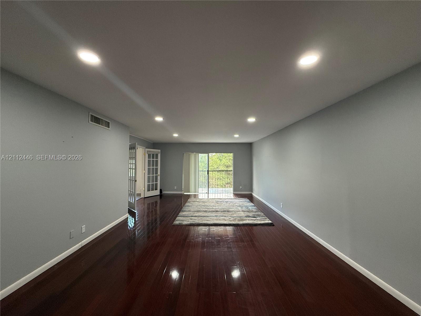 Interior room featuring dark wood-finish flooring, recessed lighting, and a glass-paneled sliding door opening to a balcony Interior room featuring dark wood-finish flooring, recessed lighting, and a glass-paneled sliding door opening to a balcony
