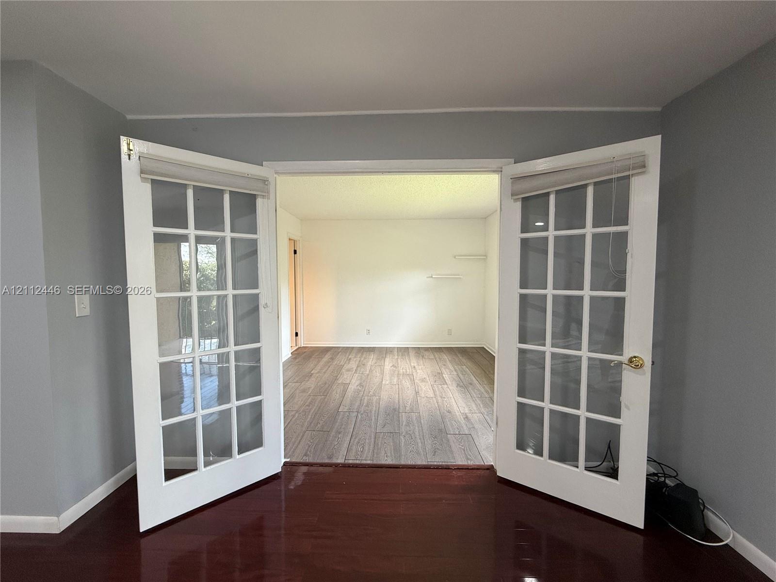 Double glass-paned doors featuring white frames, brass-finish hardware, and built-in blind fixtures, accented by wood-finish flooring