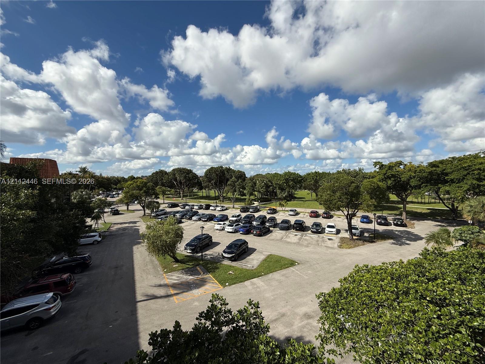 Asphalt-paved parking lot with dedicated parking spaces, bordered by mature trees and landscaped green areas