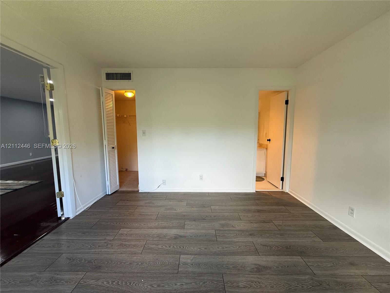 Neutral-toned interior space featuring wood-finish flooring, two doorway entries, a louvered closet door, and a textured ceiling