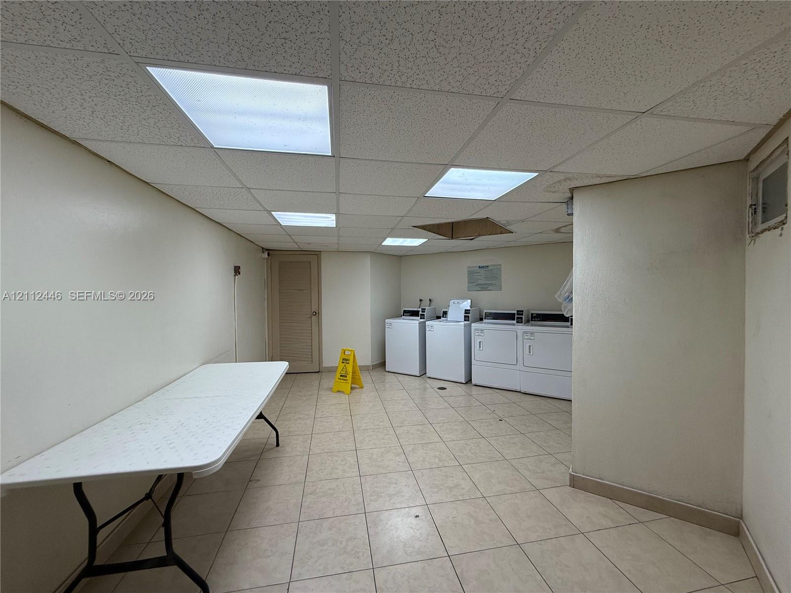 Laundry room featuring tile flooring, a drop ceiling with recessed panel lighting, and multiple washer and dryer units
