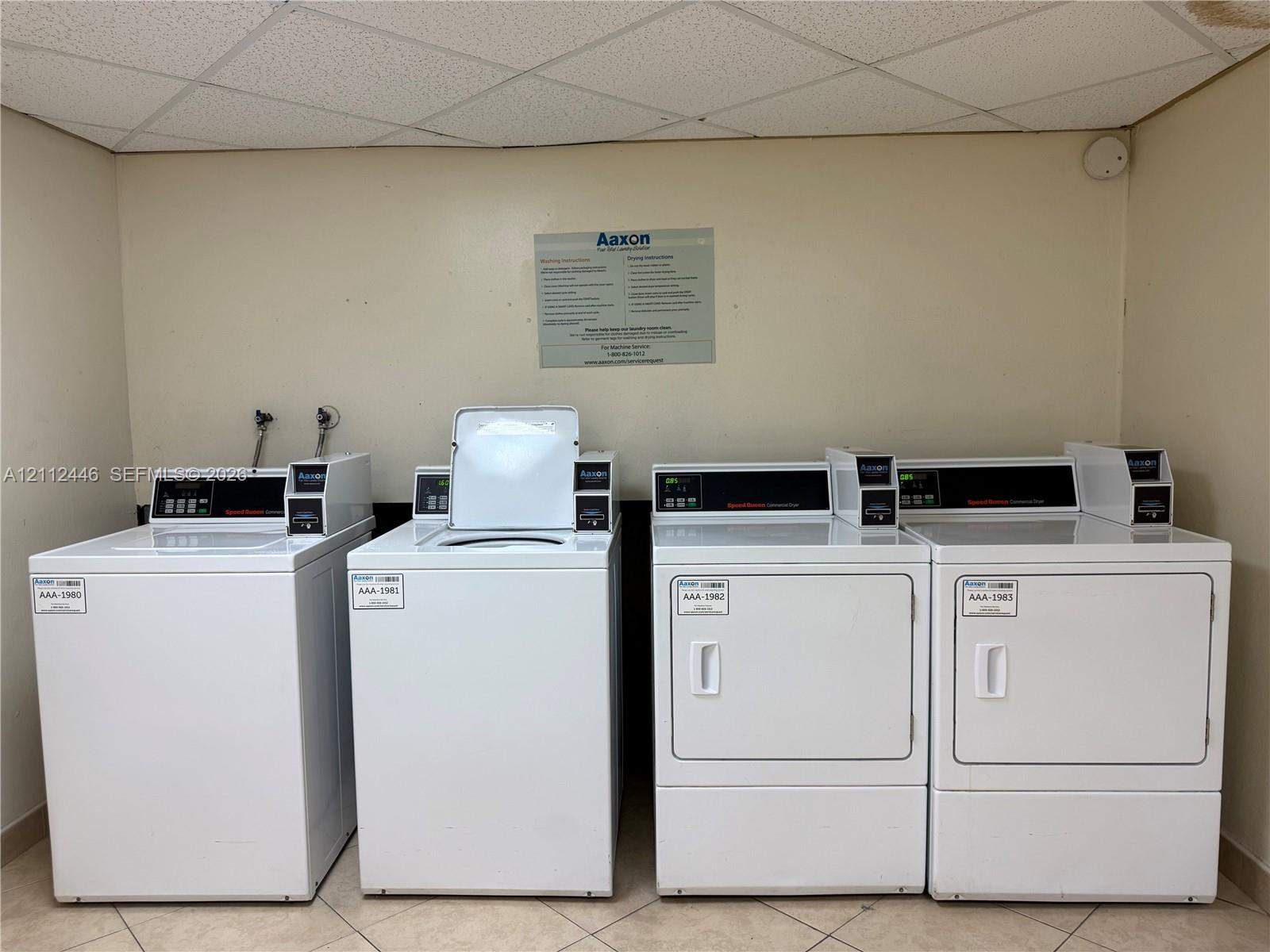 Dedicated laundry area featuring multiple white top-load washers and front-load dryers with high-capacity controls and tile flooring