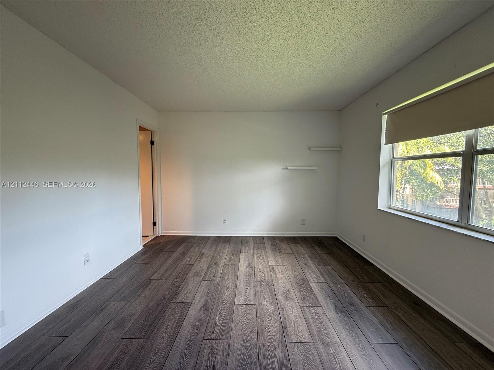 Room featuring wood-finish flooring, white walls, and built-in wall shelving Room featuring wood-finish flooring, white walls, and built-in wall shelving