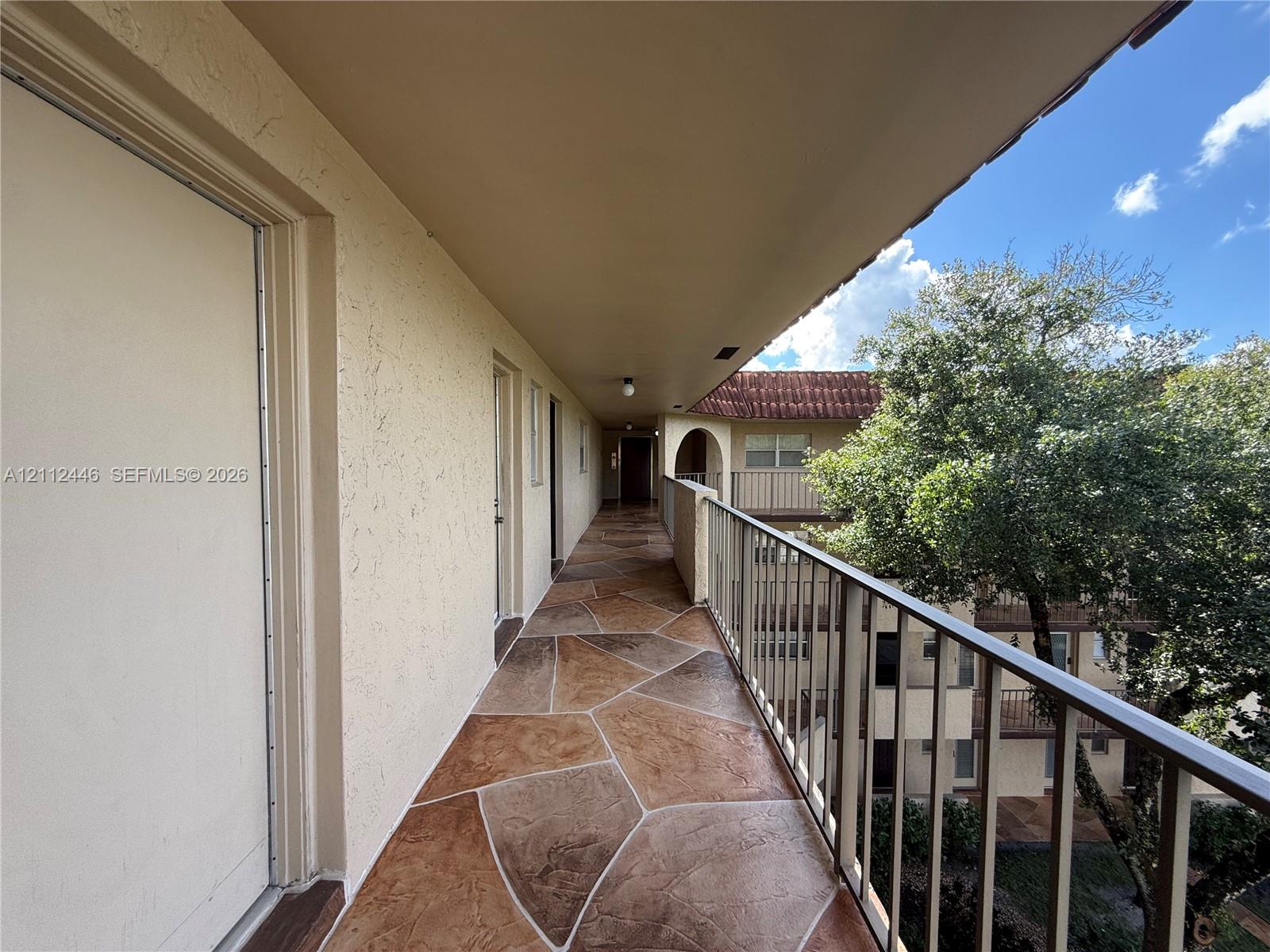 Exterior covered walkway featuring stamped concrete flooring, textured stucco walls, and metal railings