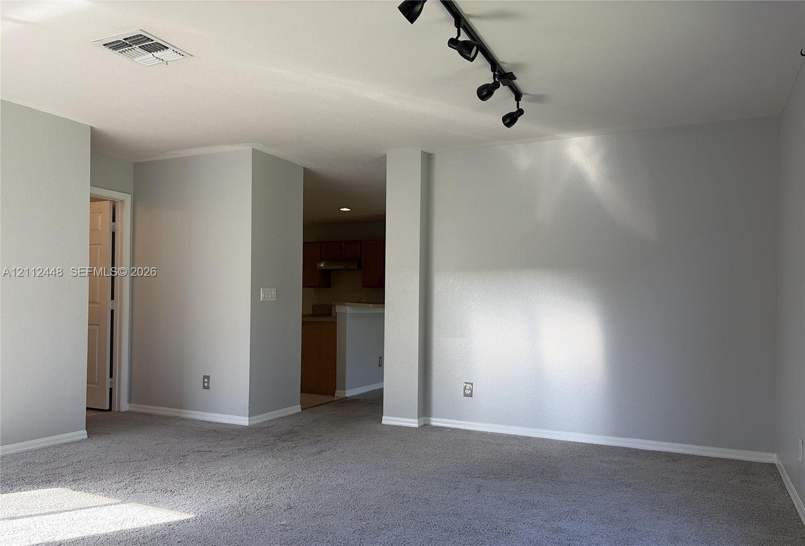 Neutral-toned interior space featuring light-colored wall paint, carpeted flooring, and a multi-head adjustable track lighting fixture
