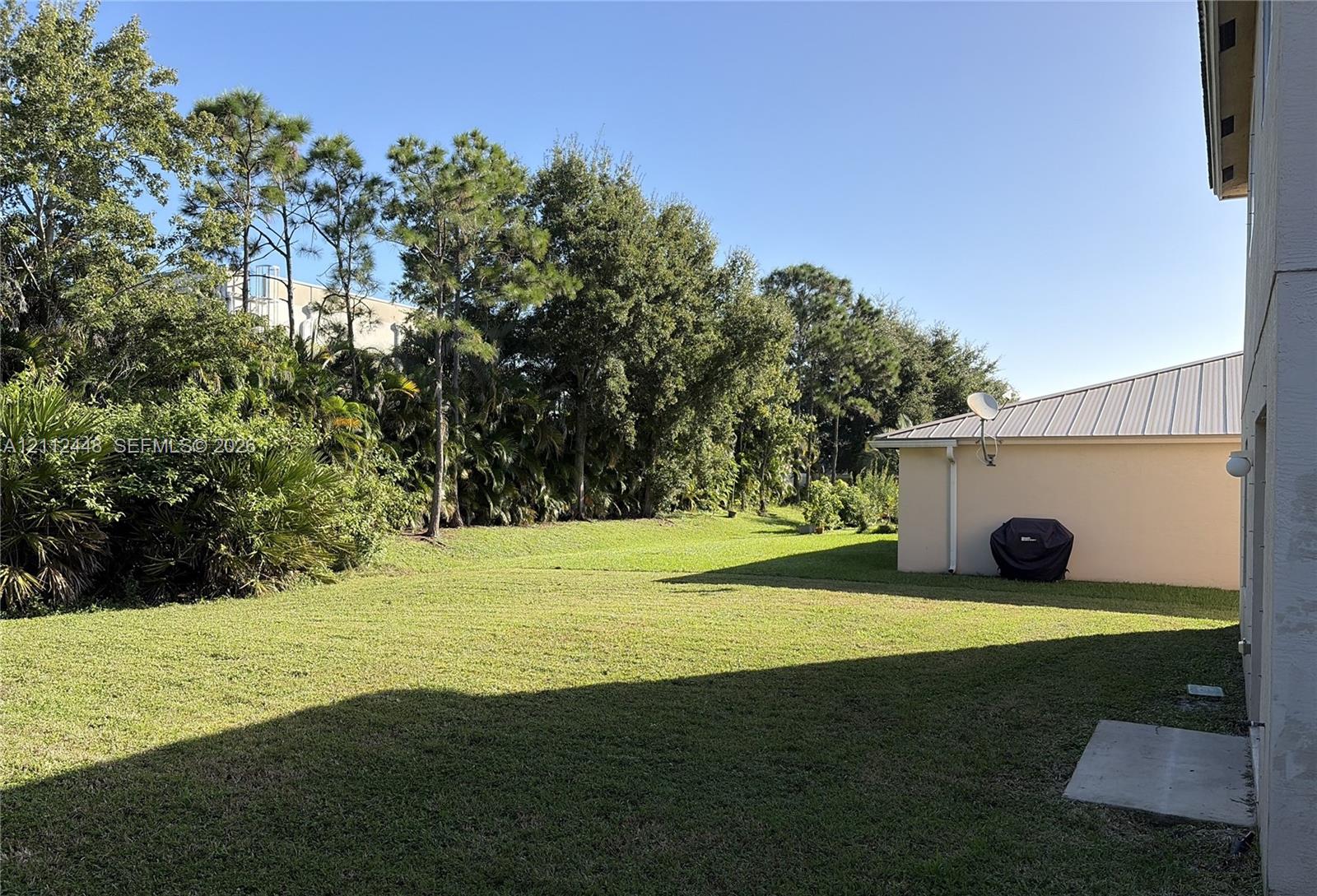 Expansive backyard featuring a large grass lawn, mature trees, and landscaping border